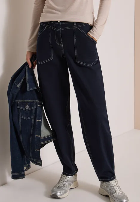 Vrouw draagt donkerblauwe baggy jeans, houdt spijkerjack vast, zilveren sneakers.