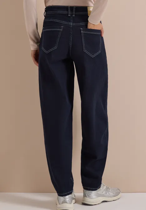 Achteraanzicht van een persoon in donkerblauwe rechte jeans en witte sneakers voor een beige achtergrond.