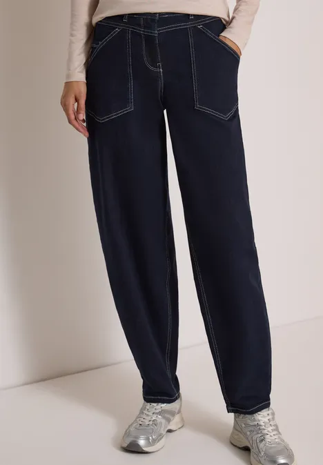 Donkerblauwe losvallende jeans met contrastnaden en zilverkleurige sneakers.