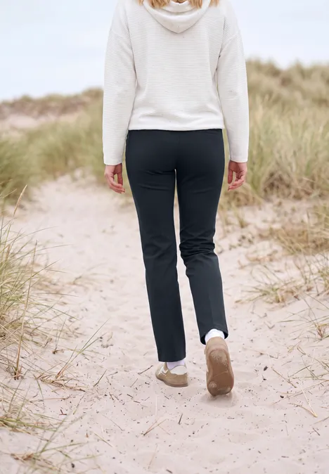 Eine Person läuft in schwarzer Hose und weißem Pulli über einen sandigen Dünenpfad mit Strandhafer.