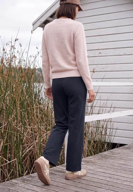 Broek met High Waist en Wide Leg pijpen in een Loose Fit pasvorm urban dark blue Een vrouw in een beige trui en donkere broek loopt over een steiger langs riet.