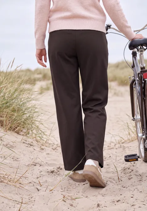 Broek met High Waist en Wide Leg pijpen in een Loose Fit pasvorm truffle brown Iemand duwt een fiets door zandduinen, draagt een zwarte broek en een roze trui.