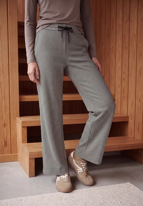 Wide Leg Hose mit Houndstooth-Muster cashmere beige Person steht auf Teppich vor Holzwand, trägt weite graue Loungehose mit Kordelzug und beige Hausschuhe