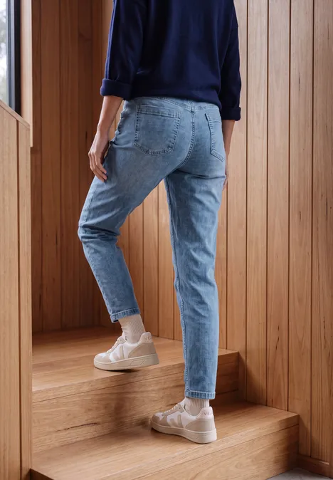 Jean taille mi-haute à Barrel Leg, coupe décontractée mid blue wash Une personne en jean bleu et baskets claires monte un escalier en bois.