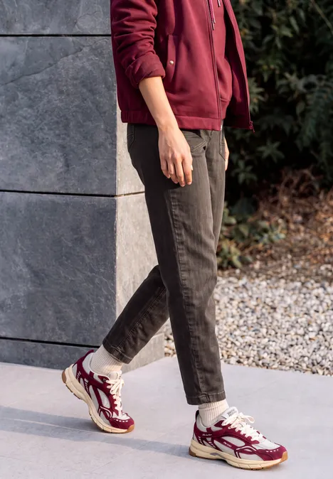 Jean « Barrel Leg » au look « garment dye » truffle brown Une personne est dehors sur un sol en pierre, porte un pantalon noir et des baskets bordeaux avec chaussettes blanches.