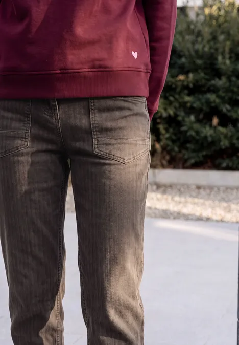 Jean « Barrel Leg » au look « garment dye » truffle brown Bas du corps d’une personne en sweat à capuche rouge et pantalon en velours marron sur trottoir.