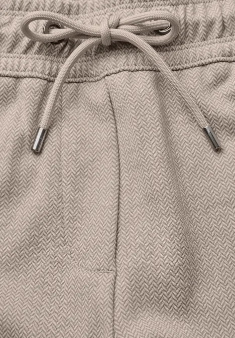 Pantalon taille mi-haute, coupe Slim Leg et style décontracté cashew beige Nahaufnahme eines beigen Sweatpants-Bunds mit Kordelzug und subtiler Fischgrätenstruktur.