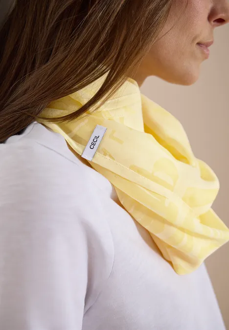 Person mit hellgelbem Schal um den Hals und hellem Oberteil, Gesicht unscharf.