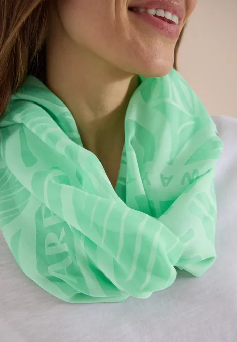 Een vrouw draagt een felgroene sjaal met subtiel patroon bij een witte top.