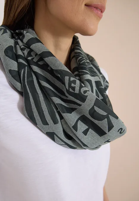 Gros plan d'une femme en T-shirt blanc portant un foulard gris à lettres foncées.