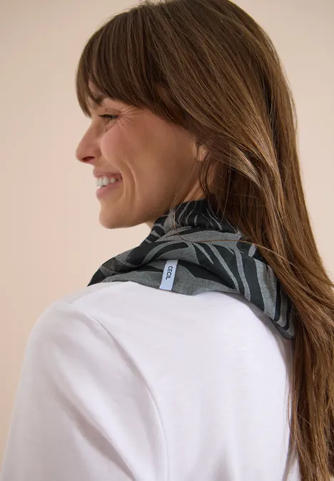 Une femme aux cheveux bruns porte autour du cou un foulard noir à motifs, le visage flouté.