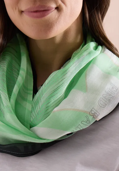 Gros plan d’une femme souriante portant un foulard vert et blanc.