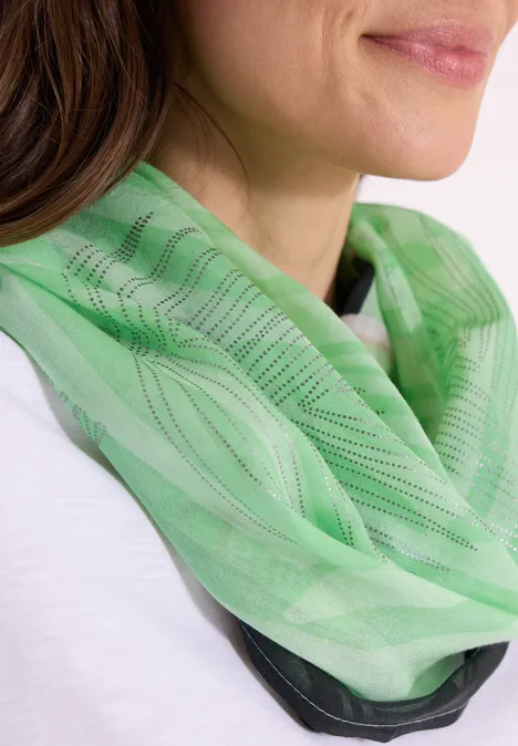 Une femme porte un foulard vert à motifs autour du cou.
