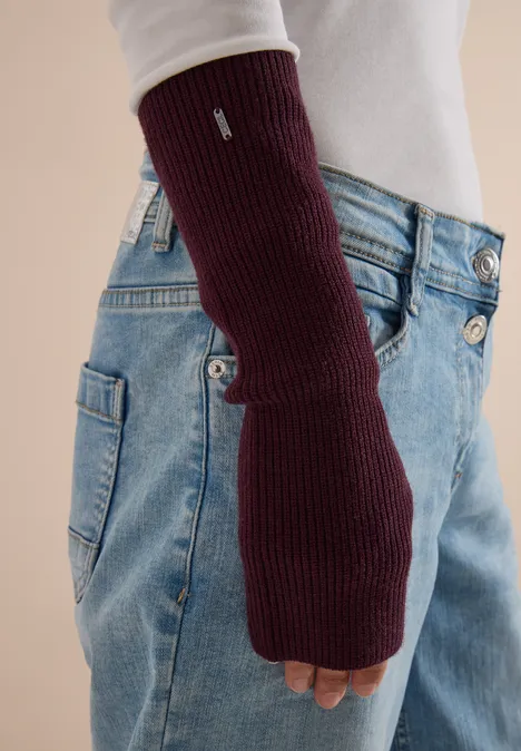 Weinrote, fingerlose Handschuhstulpe aus Rippstrick, getragen zu blauen Jeans.