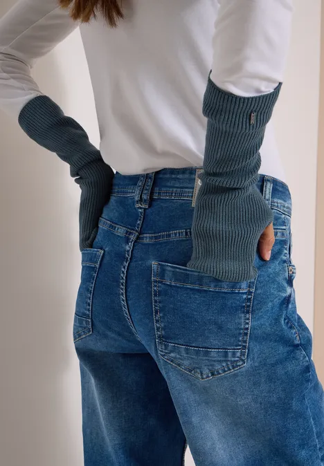 Person trägt lange, grüne, fingerlose Handschuhe und blaue Jeans, Rückansicht.