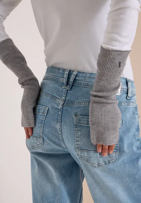 Person in blauer Jeans und grauen, fingerlosen Handschuhen, Hände auf den Hüften