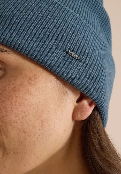 Seitenaufnahme einer Person mit Sommersprossen und blauer Strickmütze