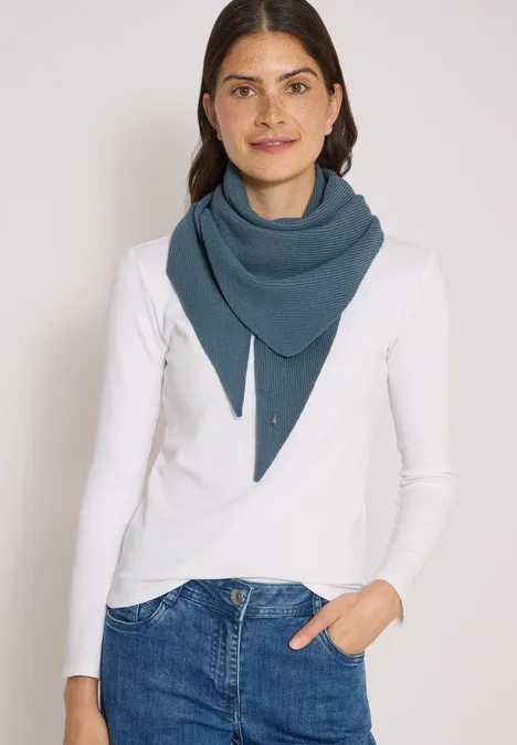 Frau in weißem Langarmshirt trägt blaues Dreieckstuch lächelnd vor hellem Hintergrund