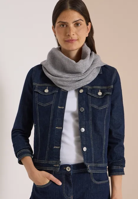 Frau mit dunklen Haaren trägt blaue Jeansjacke und grauen Schal.
