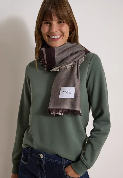 Vrouw met groene trui en grijze sjaal lacht naar de camera.