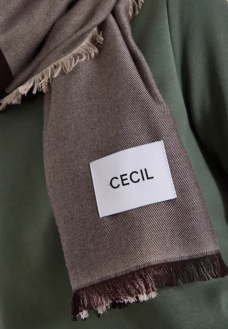 Een bruine sjaal met franjes en een wit label met de tekst ‘CECIL’.
