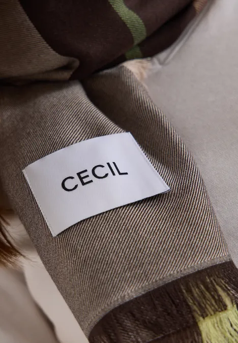 Close-up van een beige kledingstuk met een wit label en de zwarte opdruk CECIL.