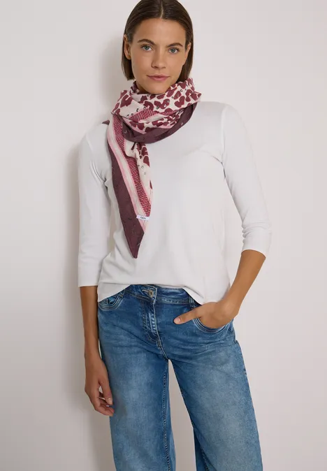 Dreieckstuch mit Leo-Muster berry red Frau in weißem Langarmshirt, blauen Jeans und gemustertem Schal steht mit einer Hand in der Hosentasche.