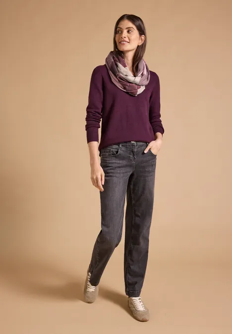 Loop-Schal mit Argyle-Muster berry red Eine Frau steht in lässiger Pose in dunkelgrauer Hose, lila Pullover und buntem Schal vor beigem Hintergrund.