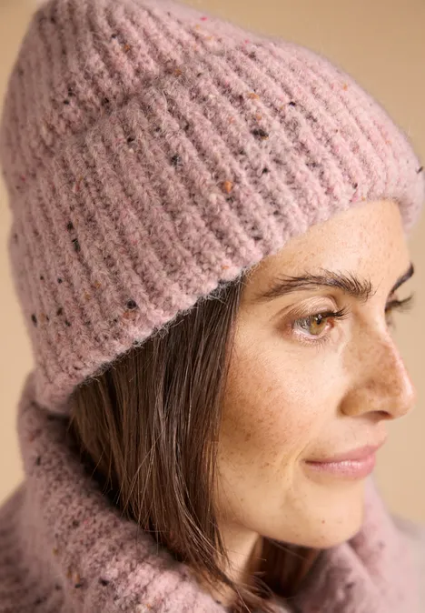 Frau mit rosa Strickmütze und -pullover, braunes Haar und Sommersprossen, Seitenansicht vor hellem Hintergrund