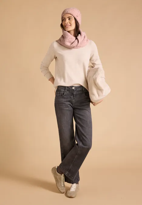 Loop-Schal mit Wollanteil und Melange-Muster neps rose fog melange Frau in beigem Pullover, schwarzen Jeans, weißen Sneakers und rosa Mütze mit Schal vor beigem Hintergrund.