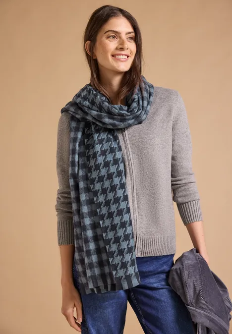 Kuscheliger Schal mit Fransen und Muster dark navy blue Frau in grauem Pullover, trägt einen blau-schwarzen Hahnentritt-Schal und hält eine Jacke, lächelt.