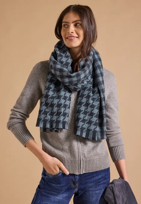 Kuscheliger Schal mit Fransen und Muster dark navy blue Frau in grauem Pullover, Jeans und kariertem Schal, hält dunkelblauen Mantel