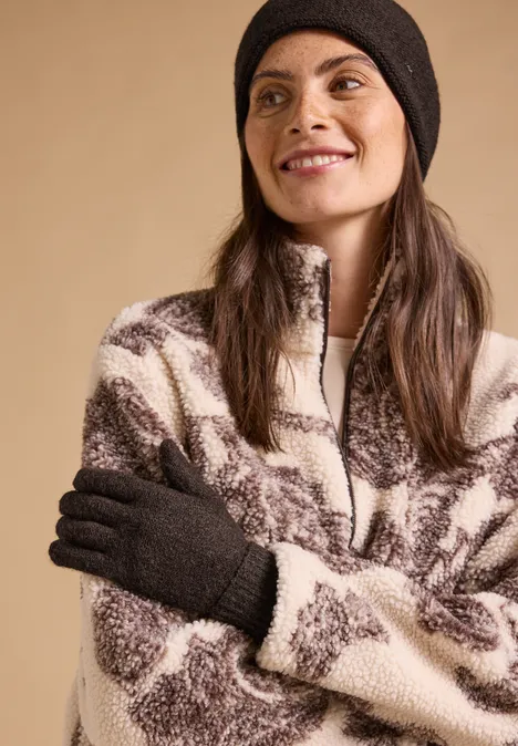 Handschuhe in Melange-Optik choco sauce brown melange Lächelnde Frau in flauschiger, braun-weißer Fleecejacke mit schwarzer Mütze und Handschuhen vor beigem Hintergrund.