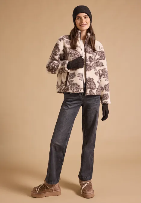 Handschuhe in Melange-Optik choco sauce brown melange Frau trägt gemusterte Fleecejacke, Mütze, Handschuhe, Jeans und Stiefel vor beigem Hintergrund.