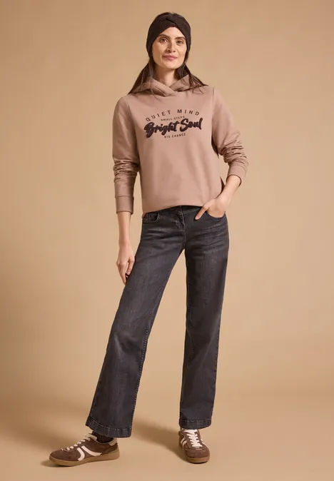 Stirnband in Melange-Optik choco sauce brown melange Frau in beigem Hoodie, weiten Jeans und Sneakers vor schlichtem Hintergrund.