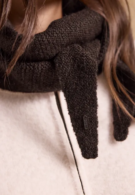 Nahaufnahme einer Person mit grob gestricktem braunem Schal und hellem Mantel