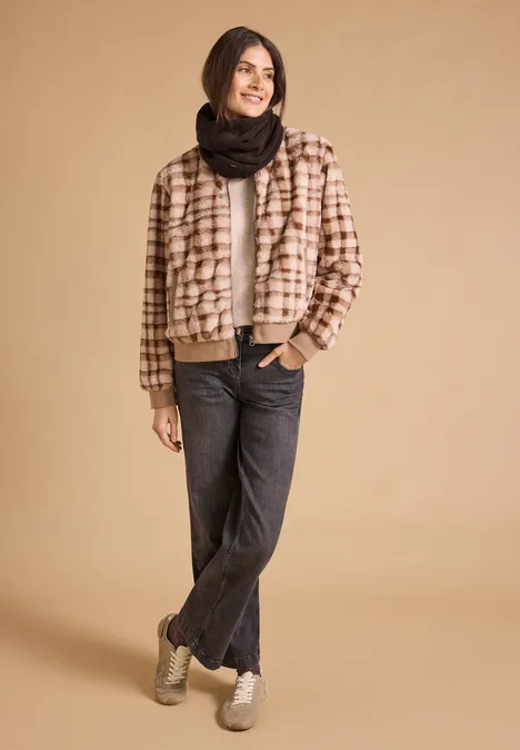 Loop-Schal in Melange-Optik choco sauce brown melange Frau im karierten Bomberjacke, schwarzem Schal, Jeans und Sneakers vor beige Hintergrund.