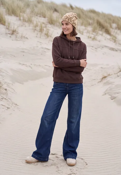 Jeune femme en sweat à capuche et bonnet debout dans les dunes.