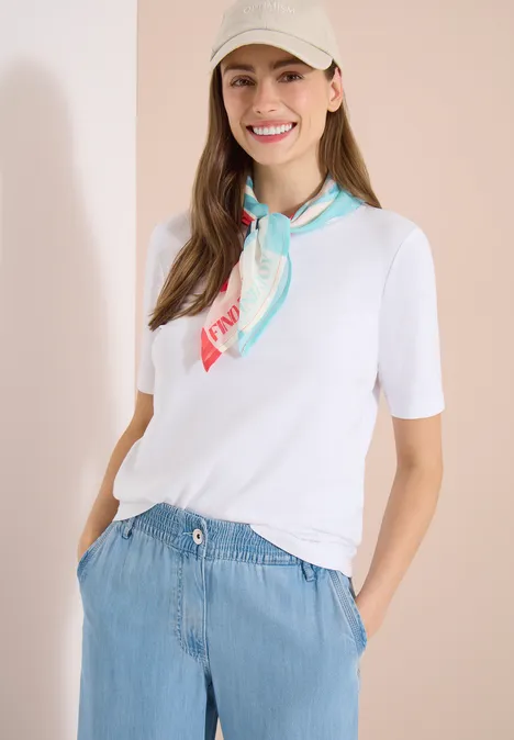 Eine Frau trägt ein weißes T-Shirt, einen bunten Seidenschal und eine hellblaue, hochtaillierte Hose.