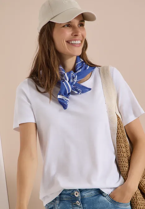 Persoon in wit t-shirt, blauwe sjaal, pet en strooien tas.