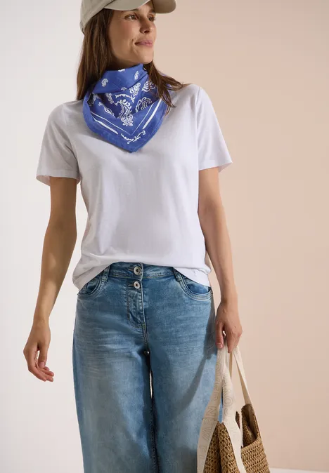 Vrouw in wit T-shirt, blauwe bandana om de hals, losse jeans en met een linnen tas.