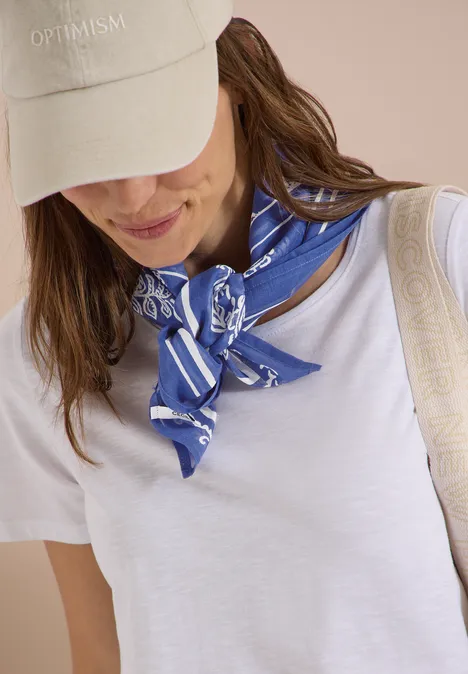 Persoon in wit T-shirt met blauwe, gemusterd zijden sjaal, wazig gezicht, minimalistische look.