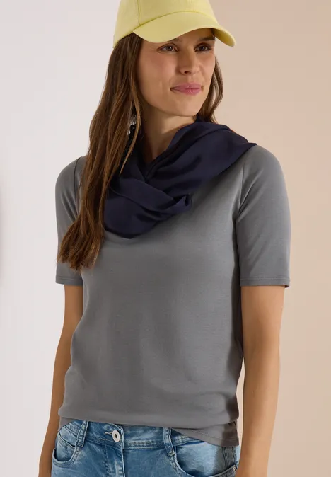Effen Loop-sjaal urban dark blue Frau in grauem T-Shirt, Jeans, gelber Cap und locker um den Hals geschlungenem dunklem Halstuch.