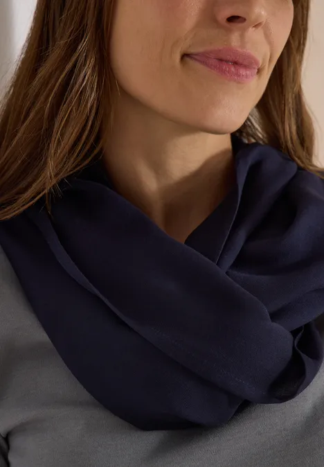 Effen Loop-sjaal urban dark blue Eine Frau mit langen braunen Haaren trägt einen dunkelblauen, rundgestrickten Schal über einem grauen Oberteil.