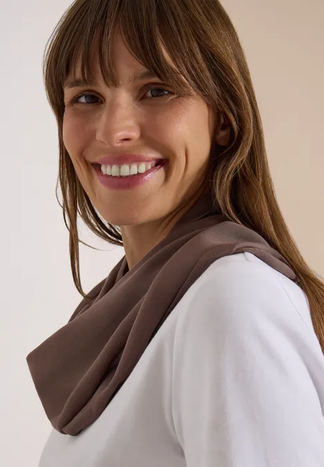 Effen Loop-sjaal urban taupe Lächelnde Frau mit braunen Haaren, die weißen Pullover und braunen Schal trägt.