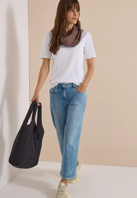Effen Loop-sjaal urban taupe Frau in weißem T-Shirt, weiten Jeans und Halstuch trägt große schwarze Tasche, steht vor hellem Hintergrund.