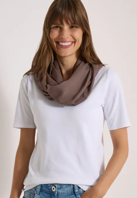 Effen Loop-sjaal urban taupe Lächelnde Frau mit weißem T-Shirt und taupefarbenem Schlauchschal vor hellem Hintergrund.
