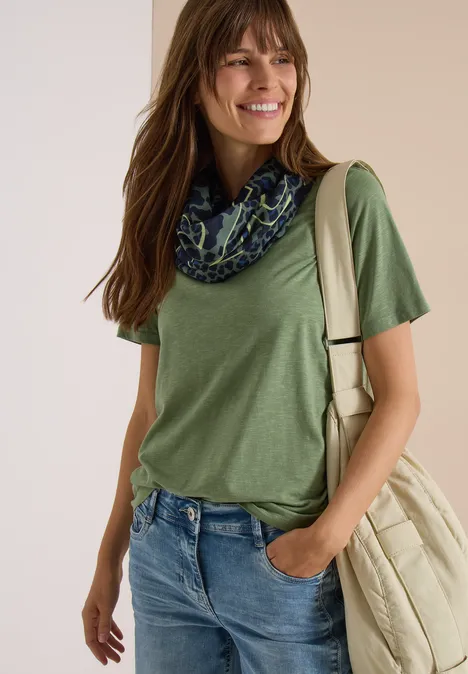 Loop-sjaal met luipaardprint dried olive green Eine lächelnde Frau in grünem T-Shirt, Jeans und Schal trägt eine beige Tasche über der Schulter.