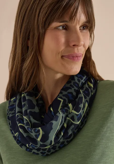 Loop-sjaal met luipaardprint dried olive green Nahaufnahme einer Frau mit braunen Haaren, die einen dunkelblauen Schal mit grünem Muster trägt.
