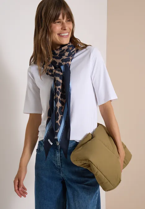 Frau in weißem T-Shirt mit blau gemustertem Schal und grünem Kissen in der Hand.